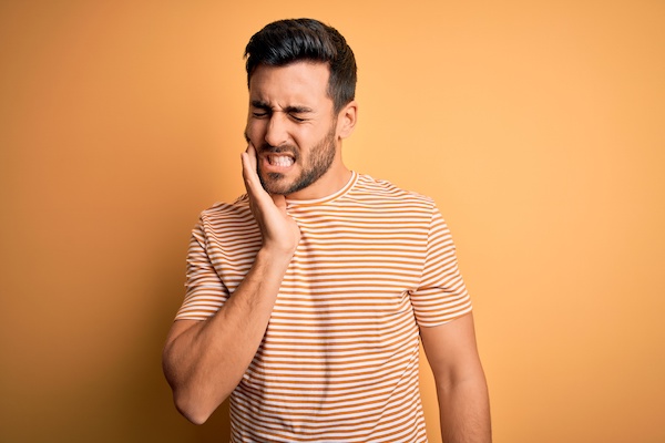 young man grimacing with toothache, orange background